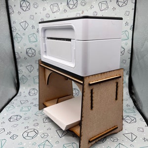 May include: A white printer sits on a wooden stand with a shelf. The stand is made of light brown wood and has a simple design.