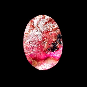 May include: An oval-shaped gemstone with a polished, reflective surface. The stone features a vibrant mix of deep magenta and bright pink hues, contrasted by dark, irregular black inclusions and translucent, crystalline white areas throughout.
