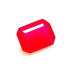 Puede incluir: Un objeto rectangular rojo brillante con un interior blanco y hueco. El objeto tiene un diseño geométrico facetado y se encuentra sobre un fondo blanco liso. La forma se asemeja a una gema o a un elemento decorativo.