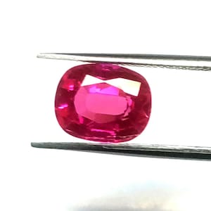 Może przedstawiać: Owalny, żywy różowy kamień szlachetny, trzymany przez pęsetę, jest pięknym przykładem rubinu.