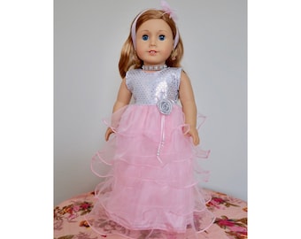 Puede incluir: Un vestido rosa y plateado con un corpiño de lentejuelas y una falda de tul. El vestido tiene un adorno de flor plateada y un cinturón de cuentas plateadas. El vestido está diseñado para una muñeca.