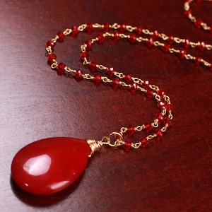 May include: A red gemstone pendant necklace with a gold chain and red crystal beads.