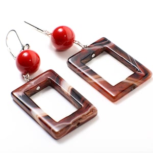 May include: A pair of dangle earrings with red agate and brown agate stones. The earrings have a silver hook and a red bead.