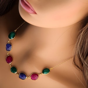 May include: A gold chain necklace with five oval-shaped gemstones. The gemstones are green, blue, red, green, and blue.