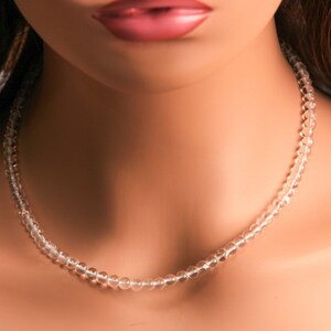 May include: A clear crystal beaded necklace on a mannequin. The necklace is made of small, round beads that are strung together on a thin cord.