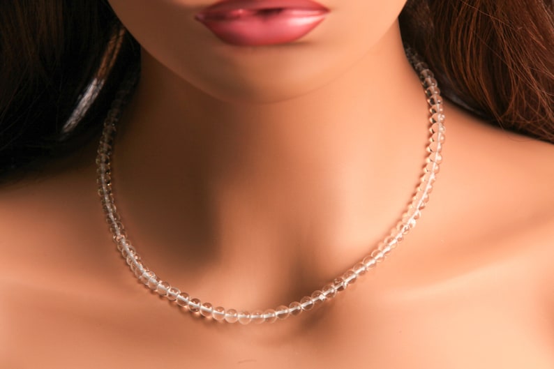 May include: A clear crystal beaded necklace on a mannequin. The necklace is made of small, round beads that are strung together on a thin cord.