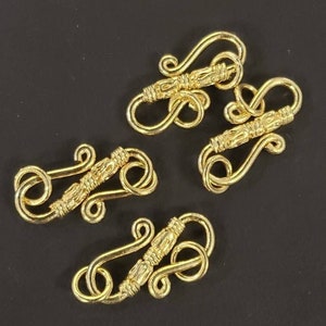 May include: Four gold-toned metal clasps with intricate designs. Each clasp has two loops, one larger than the other, connected by a decorative bar.