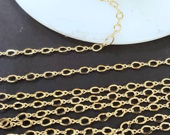 May include: A spool of gold-coloured chain with oval links. The chain is laid out in rows on a black surface.