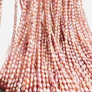 May include: Multiple strands of pink freshwater pearls. The oval-shaped pearls have a glossy finish, with colours ranging from pale pink to a deeper rose. The pearls are strung together, creating a flowing, cascading effect.