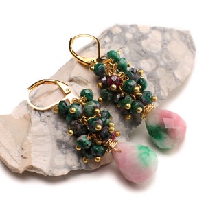 May include: Gold earrings with green and pink gemstone drops. The earrings feature a cluster of small green and pink gemstones, with a larger pink and green gemstone drop hanging from each earring.
