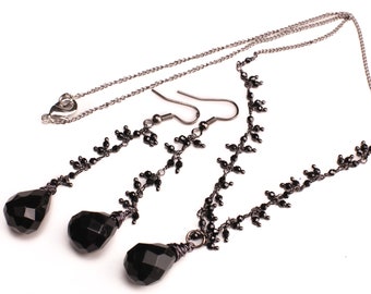 May include: A black necklace and earrings set with teardrop-shaped black gemstone pendants and delicate black bead chains.