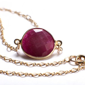 May include: A gold chain necklace with a large, round, faceted ruby gemstone pendant.