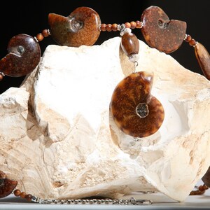 May include: A necklace made of brown ammonite fossils and wooden beads. The necklace is displayed on a white rock.