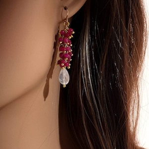 May include: Gold earrings with a cascade of ruby red beads and a single teardrop-shaped moonstone dangle.