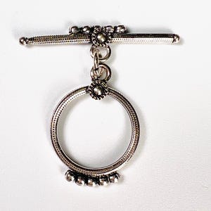 May include: Silver toggle clasp with a round, decorative ring and beaded accents.