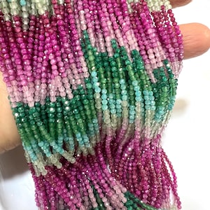 May include: Strands of faceted gemstone beads in shades of pink, green, and blue. The beads are small and strung together, creating a colorful and textured display. The gemstones are held in a hand.