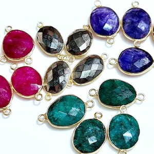 May include: Assortment of oval-shaped gemstone connector charms with gold-toned metal accents. The charms feature various colors, including red, green, blue, and black.