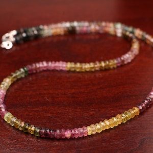 Puede incluir: Un collar de piedras preciosas multicolores con pequeñas cuentas facetadas en tonos de verde, rosa y amarillo. El collar está hecho de plata y tiene un diseño simple y elegante.