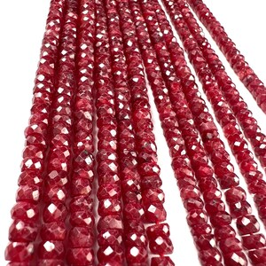 Peut inclure: Gros plan de plusieurs brins de perles de pierres précieuses rouge foncé à facettes. Les perles sont enfilées ensemble, créant un effet de cascade. Les perles ont un aspect brillant et poli, reflétant la lumière. Le thème général est les bijoux et les fournitures d'artisanat.