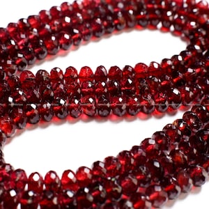 May include: A strand of deep red garnet beads, faceted and polished, strung together to create a necklace or bracelet. The beads are uniform in size and shape, with a smooth, glossy finish.