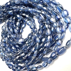 May include: A strand of blue kyanite gemstone beads, oval shaped and smooth, with a light blue colour and a translucent appearance.