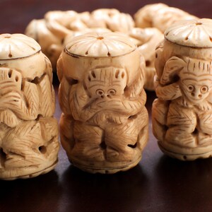 May include: Three carved ivory figurines of monkeys, each with a different pose representing the "See No Evil, Hear No Evil, Speak No Evil" proverb. The monkeys are carved in a traditional style and have a light brown color.