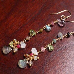 May include: A pair of gold dangle earrings with a cluster of colorful gemstones, including green, pink, blue, and purple.