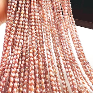 Puede incluir: Hebras de perlas de agua dulce de color rosa-marrón. Las perlas de forma ovalada están ensartadas, creando un efecto de cascada. Las perlas tienen un brillo natural y diferentes tonos de rosa y marrón. La imagen muestra varias hebras de perlas.