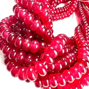 Peut inclure: Gros plan de plusieurs brins de perles rouges. Les perles sont d'un rouge profond et riche et semblent être faites d'un matériau brillant. Les perles sont enfilées ensemble, formant un motif enroulé et superposé sur fond blanc.