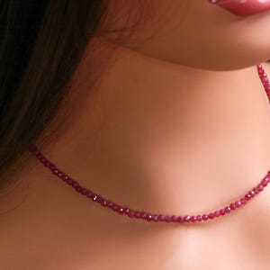 May include: A delicate ruby necklace composed of small, faceted red beads. The necklace is draped around a person's neck, showcasing the vibrant color and subtle sparkle of the gemstones. A classic piece of jewelry.
