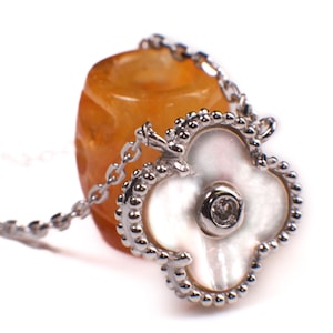 May include: A silver necklace featuring a white mother-of-pearl flower pendant with a small clear gemstone at its centre. The pendant is attached to a silver chain and a large orange gemstone.