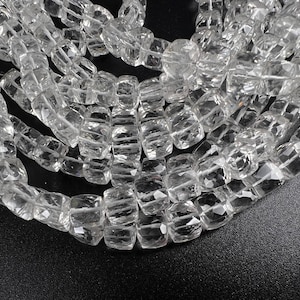 May include: Close-up of clear, faceted crystal beads strung together. The beads have a rectangular shape with cut edges, creating a sparkling effect. The beads are displayed against a dark background, highlighting their clarity. Ideal for jewelry making.