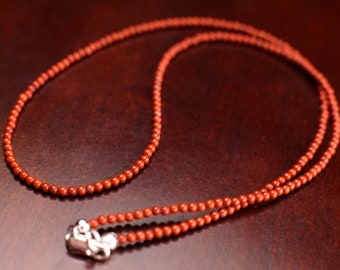 May include: A red beaded necklace with a silver clasp. The necklace is made of small, round beads and is about 18 inches long.