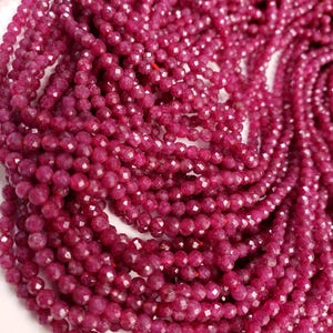 May include: A strand of faceted ruby red gemstone beads. The beads are small and round, and they are strung together on a clear thread. The beads are all the same size and shape, and they are arranged in a random order.