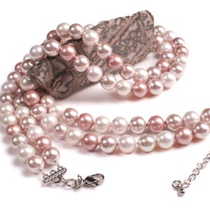 May include: A multi-strand pearl necklace with pink and white pearls. The necklace has a silver clasp and is displayed on a piece of rock.