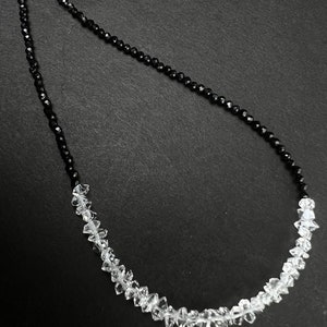 Puede incluir: Un collar de cuentas negro y blanco con cuentas negras en la mitad superior y cuentas transparentes en la mitad inferior.