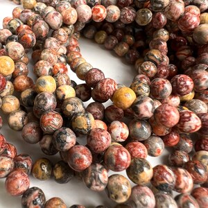 Può includere: Una collana di perline rotonde in pietra naturale multicolore. Le perline sono un mix di rosso, marrone, nero e bianco. Le perline hanno un diametro di circa 8 mm.
