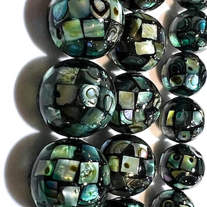 May include: A strand of round, iridescent beads made from black and green abalone shell. The beads are arranged in a row and have a mosaic-like pattern.