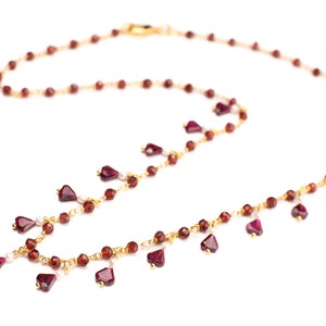 May include: A gold chain necklace with small red heart-shaped beads and small round red beads. The necklace has a dangling design with the heart-shaped beads hanging from the chain.