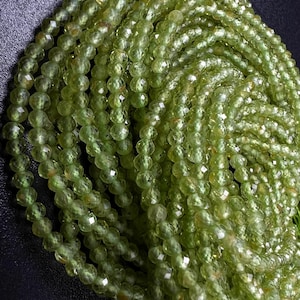 May include: A strand of green peridot beads, faceted and round, with a high-polish finish. The beads are strung on a clear thread and are ready to be used for jewelry making.