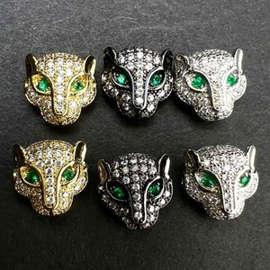 Op de afbeelding: Zes panterkopcharms met groene ogen en witte zirkonia-stenen. De charms zijn in drie verschillende metaalafwerkingen verkrijgbaar: goud, zilver en zwart.