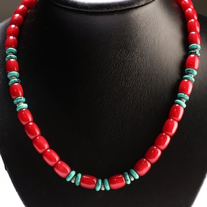 Op de afbeelding: Een rode en turquoise kralenketting op een zwarte standaard. De ketting is gemaakt van rode koraalkralen en turquoise kralen met zilveren accenten.