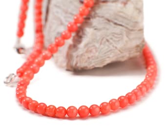 May include: A coral necklace made of small, round beads. The necklace is draped over a piece of rock.
