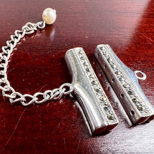 May include: A silver chain with a pearl charm attached to a pair of silver and marcasite toggle clasps.