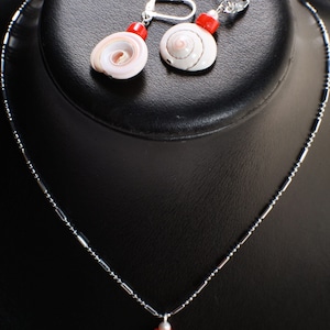 May include: A silver chain necklace with a pink and white seashell pendant and red coral beads. Matching earrings with pink and white seashells and red coral beads.