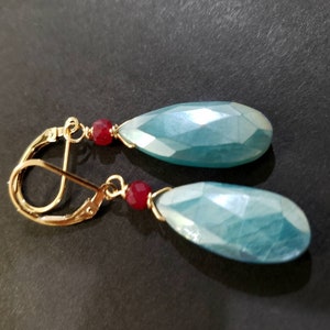Può includere: Un paio di orecchini pendenti con pietre blu a forma di lacrima e perline rosse. Gli orecchini hanno ganci dorati.