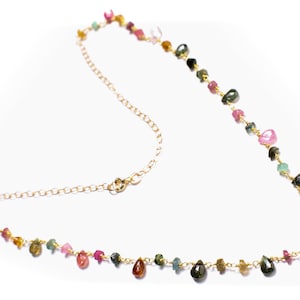 May include: A gold chain necklace featuring a selection of small, colourful gemstones. The gemstones are in shades of pink, green, and brown.