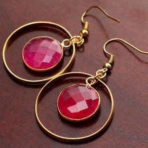 May include: A pair of gold hoop earrings with a pink gemstone in each hoop.