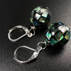 May include: A pair of silver hoop earrings with green and black iridescent shell bead dangles.