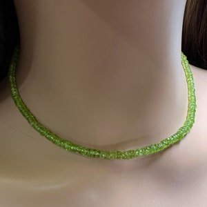 May include: A green peridot gemstone necklace. The necklace is made of small, round beads that are strung together on a thin chain.